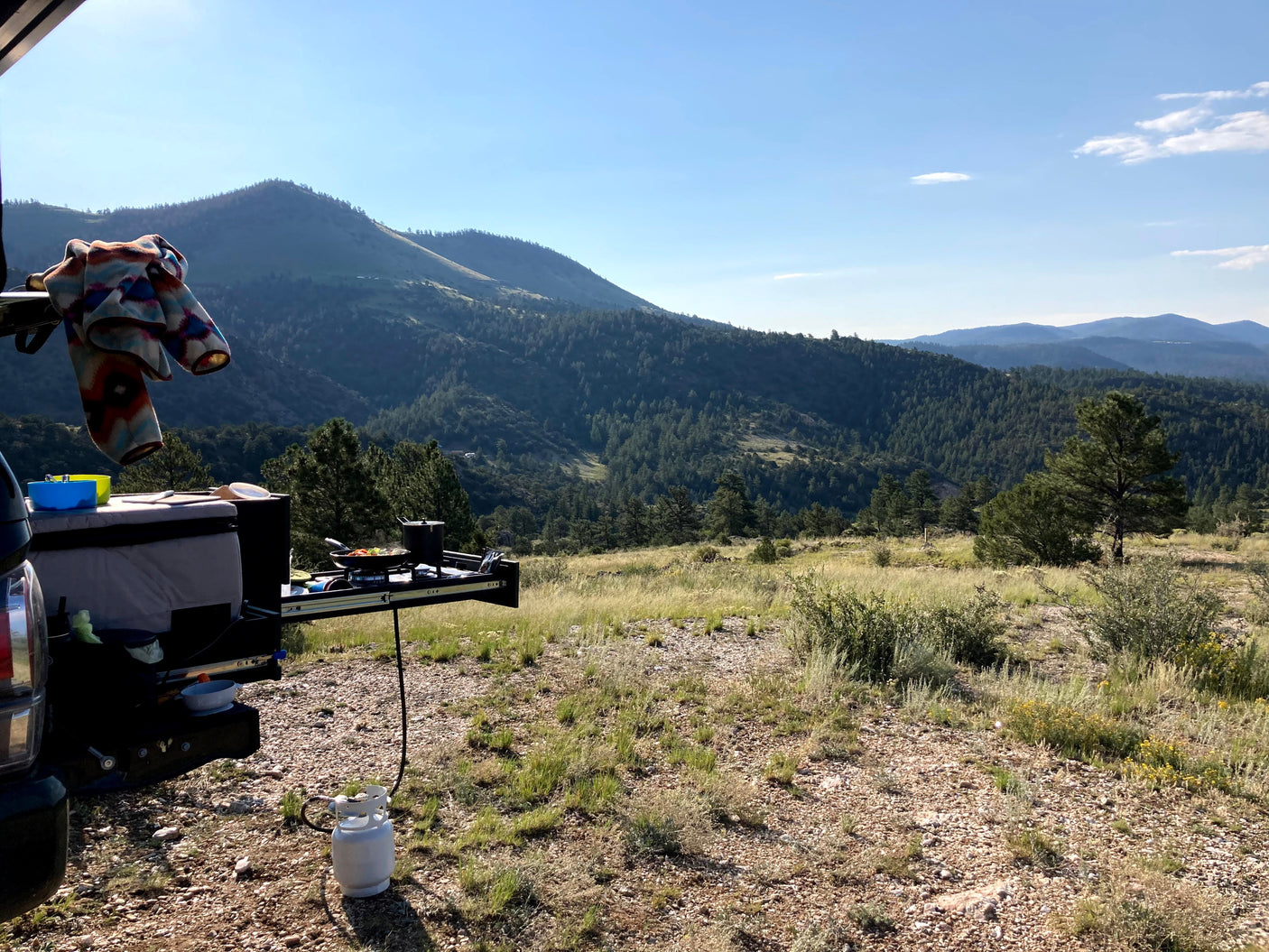 RV rental adventure: cooking outdoors with propane stove, amidst serene mountains and lush forests. Ideal camping setup.