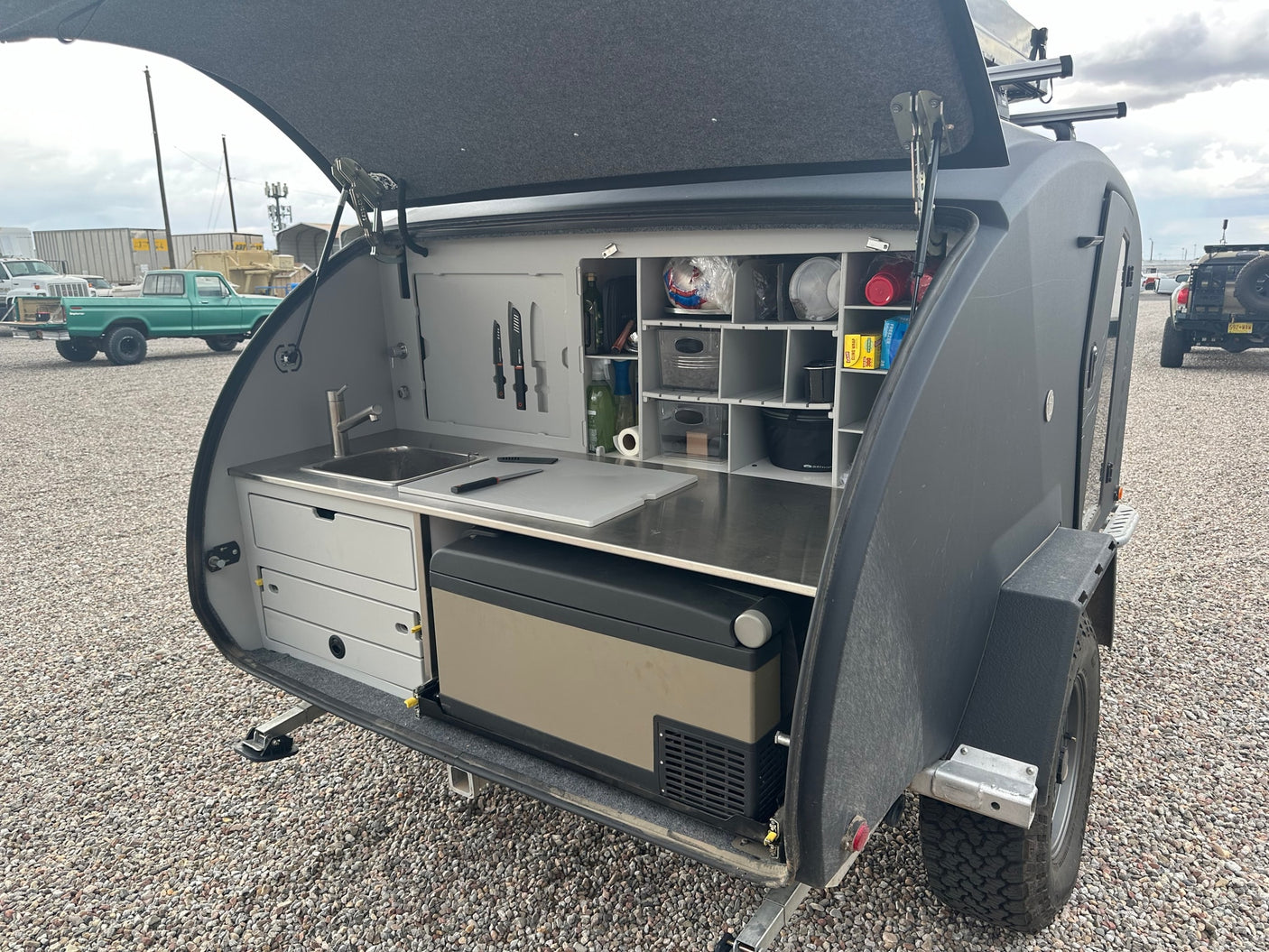 Compact RV rental: Teardrop trailer's organized outdoor kitchen with sink, fridge, and storage, perfect for camping adventures.