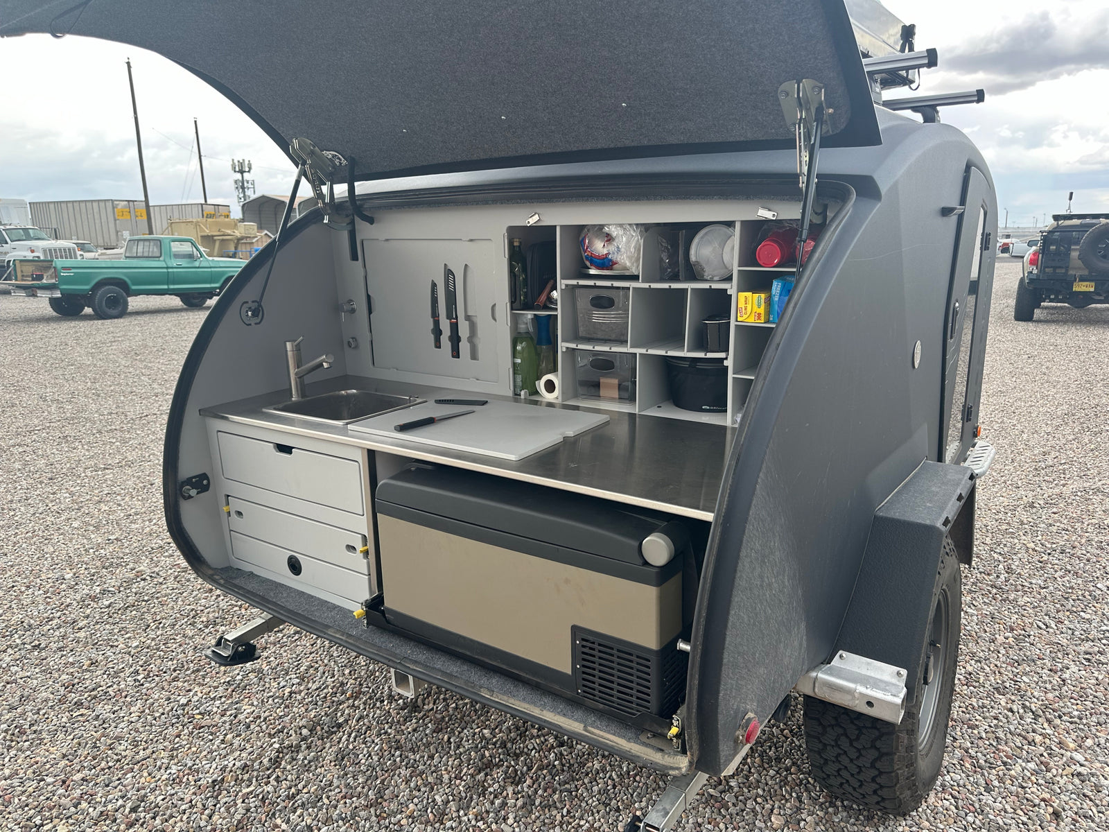 Compact RV rental: Teardrop trailer's organized outdoor kitchen with sink, fridge, and storage, perfect for camping adventures.