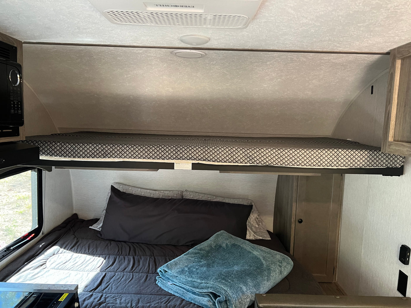 RV rental interior: a cozy sleeping area featuring a lower bed with dark bedding, an upper patterned bunk, and a microwave.