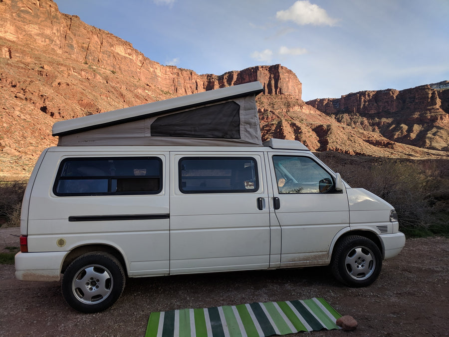 White pop-top camper van with stunning red rock mountain backdrop. Perfect for an RV rental adventure!