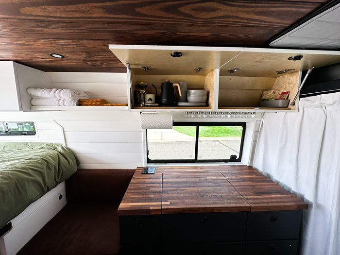 revealing its custom camper interior. Parked on a dirt road.|This RV rental showcases a cozy van interior with a bed