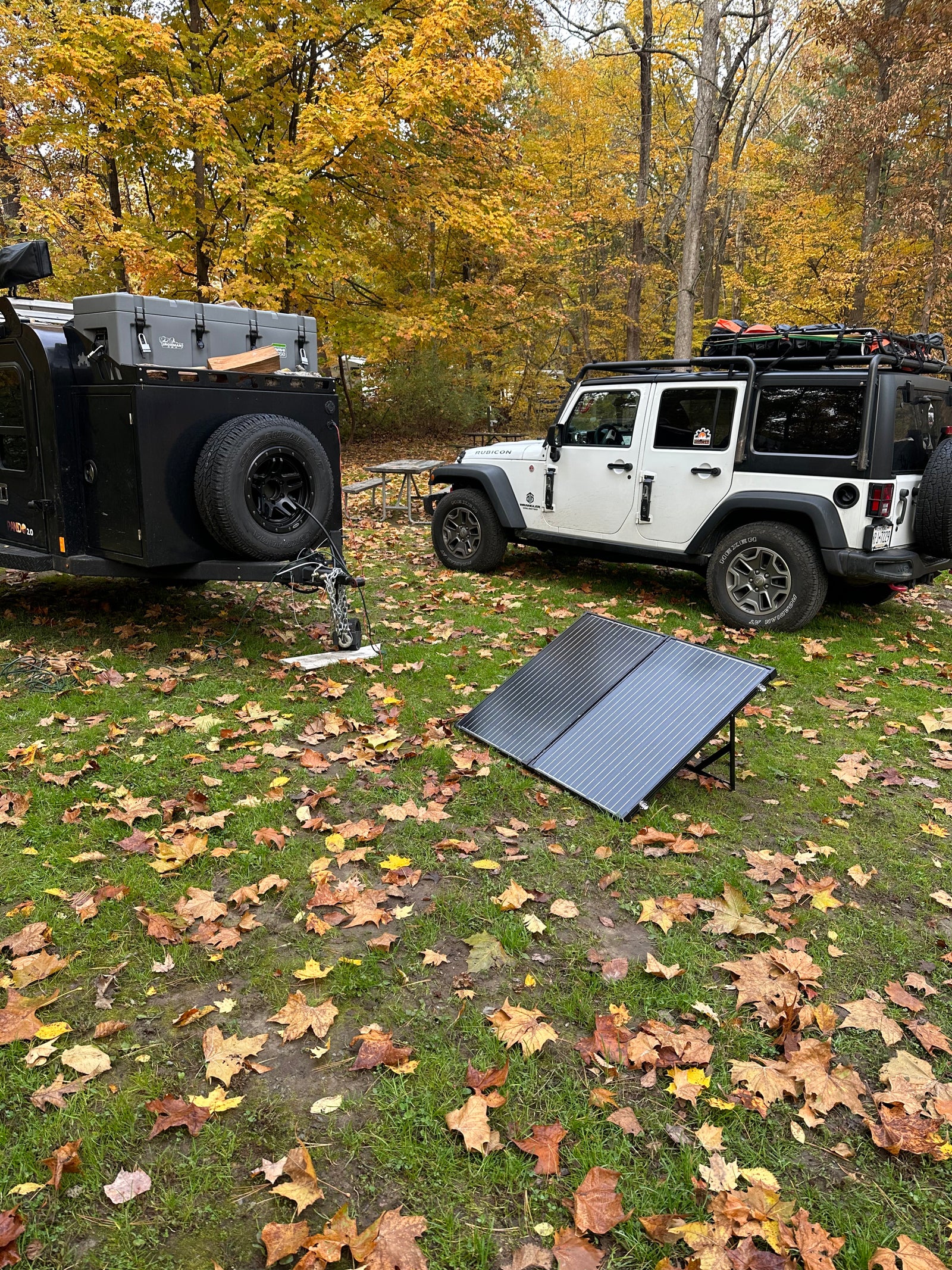 ideal as an RV rental for outdoor adventures.|RV rental setup: A black Jeep Gladiator and an adventure trailer are parked on a concrete pad by a lake in a wooded campsite.|Nighttime scene: An RV rental's illuminated rear kitchen