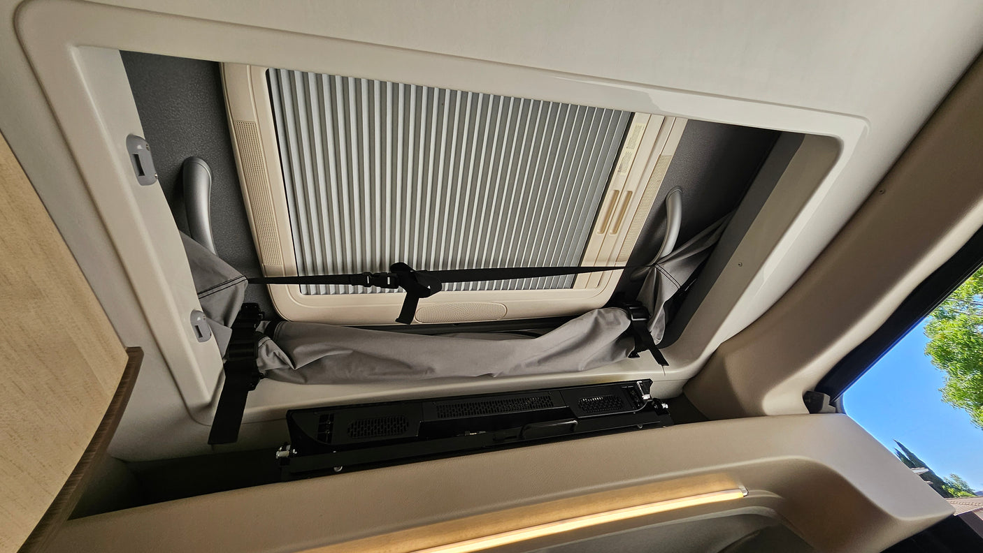 rv rental interior: overhead view of a skylight with closed blind, strapped storage, and mounted entertainment unit.