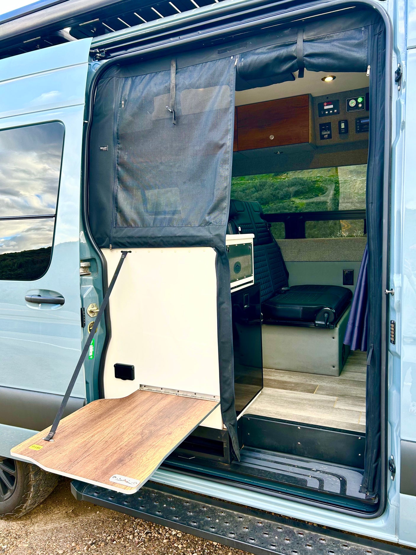 This camper van RV rental features an open side door with a mesh screen, fold-out table, and a peek inside.