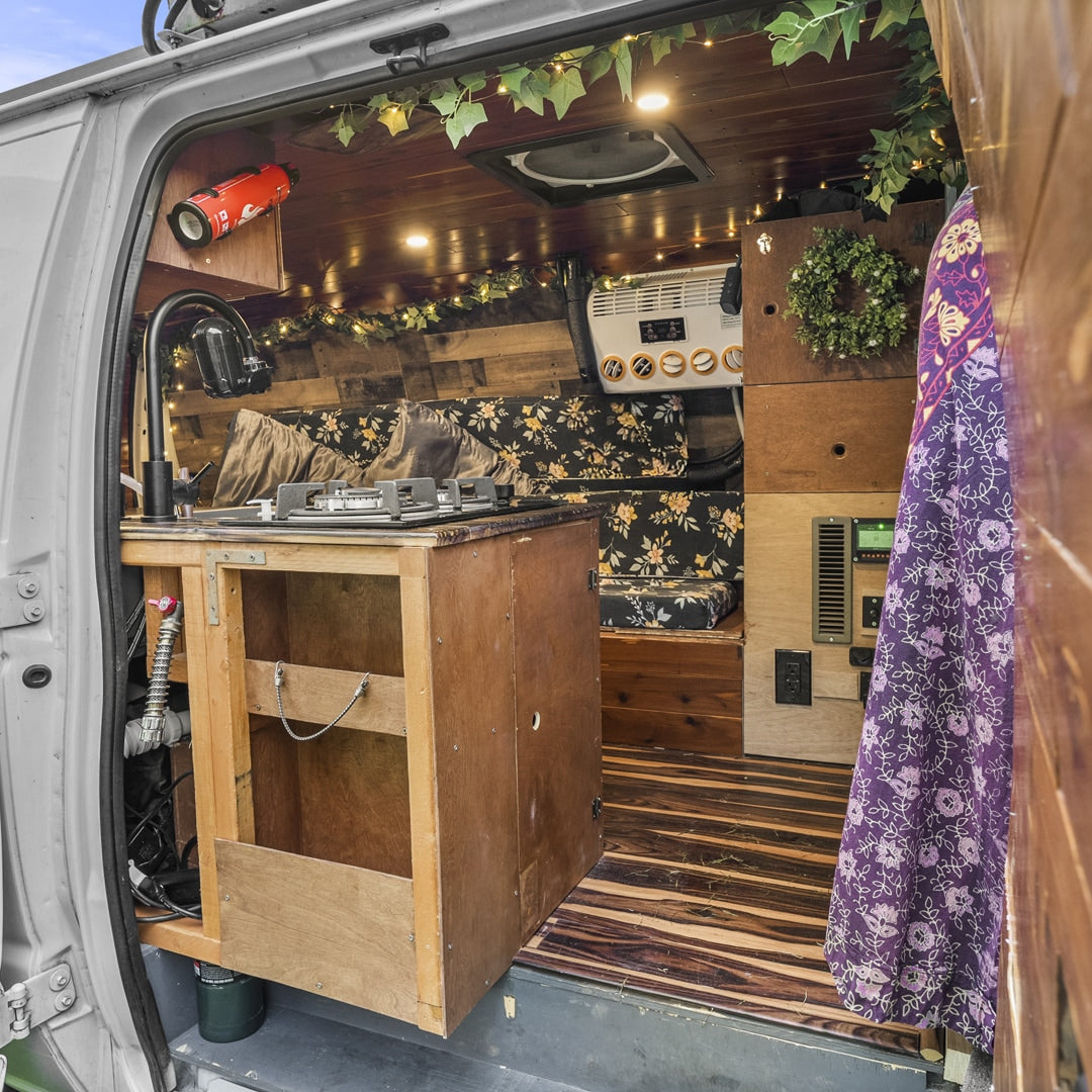 Inside this RV rental, a compact kitchen with stove, cozy seating, and wooden decor creates a homey mobile space.