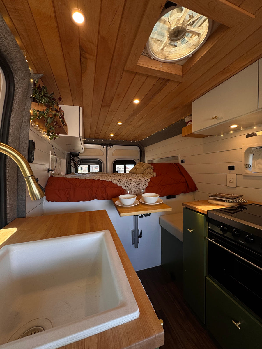 Cozy rv rental interior: wooden ceiling, built-in bed, and kitchen with sink & stove, ready for adventure.
