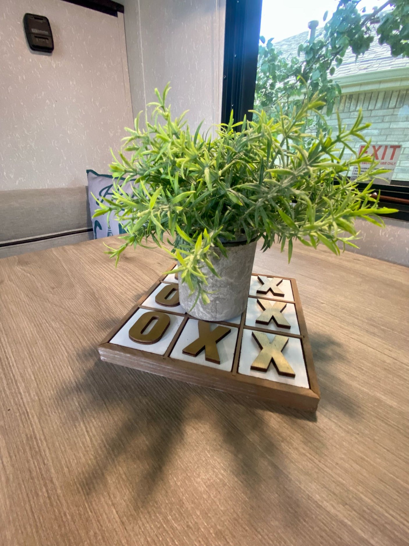 Cozy RV rental interior: faux plant on a tic-tac-toe game board, wooden table, with window view.