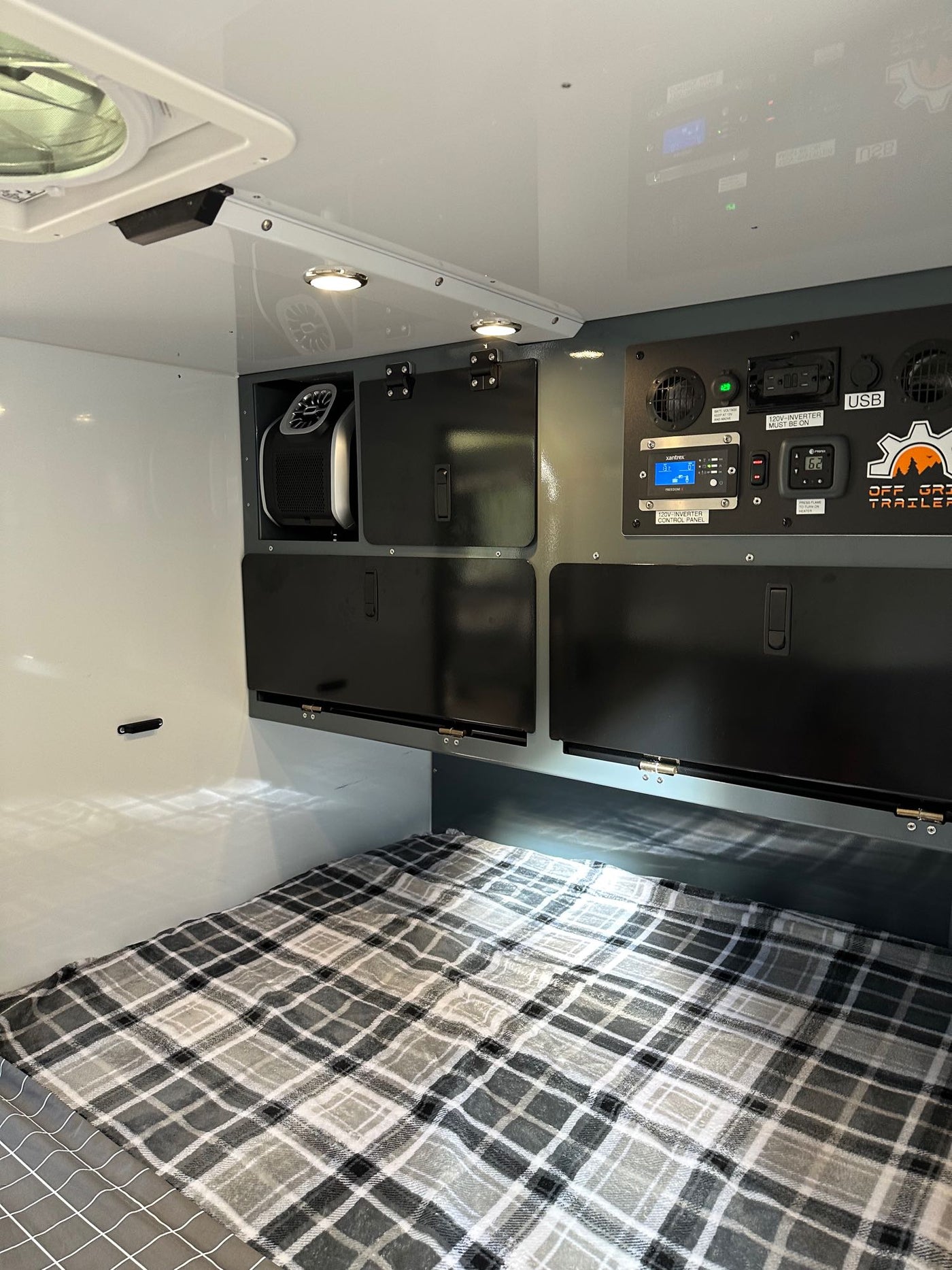 RV rental interior features a cozy bed, overhead storage, and an advanced off-grid control panel with USB access. — photo 20