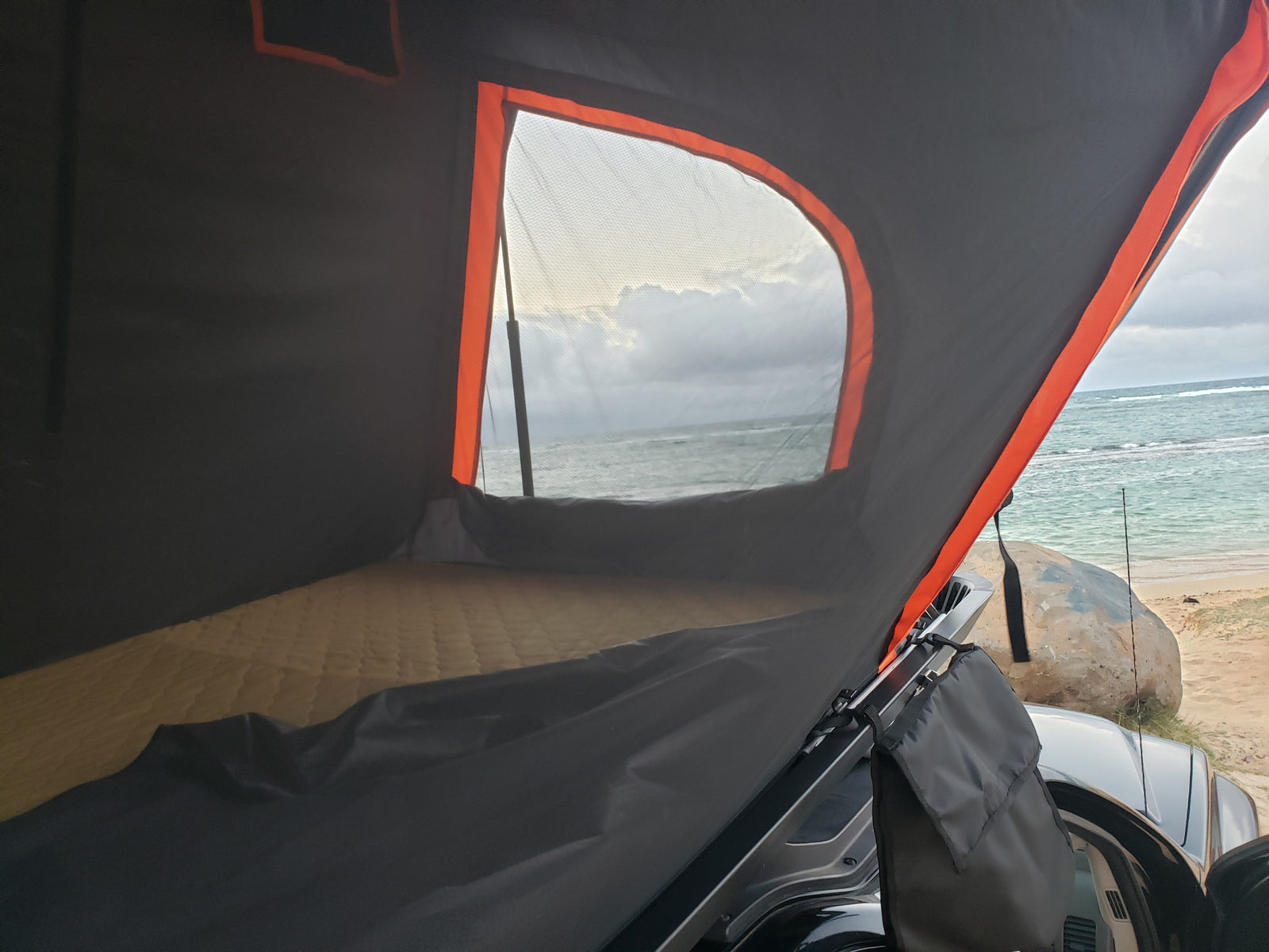Cozy rooftop tent interior with mattress, seaside view of ocean & beach. Great for your RV rental adventure!