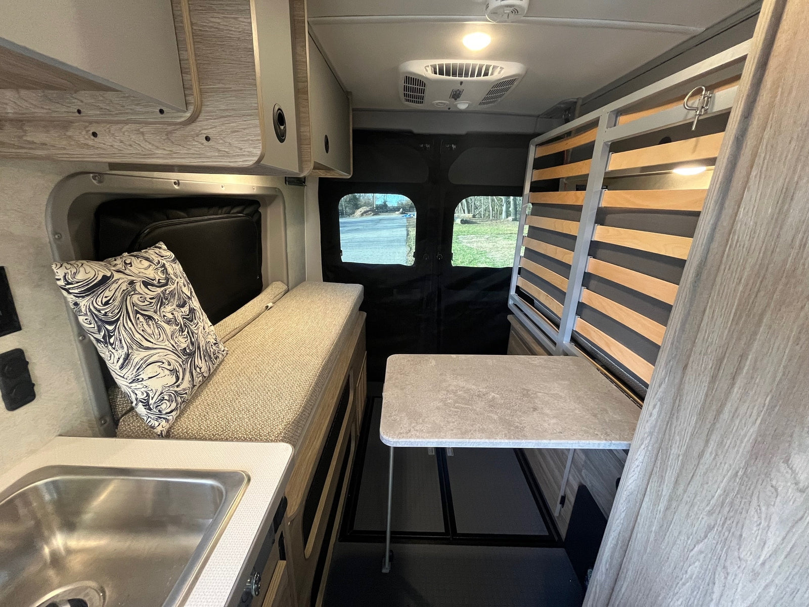 Spacious RV rental interior with kitchen sink, bench seat, table, and slatted bed frame, offering comfortable travel.