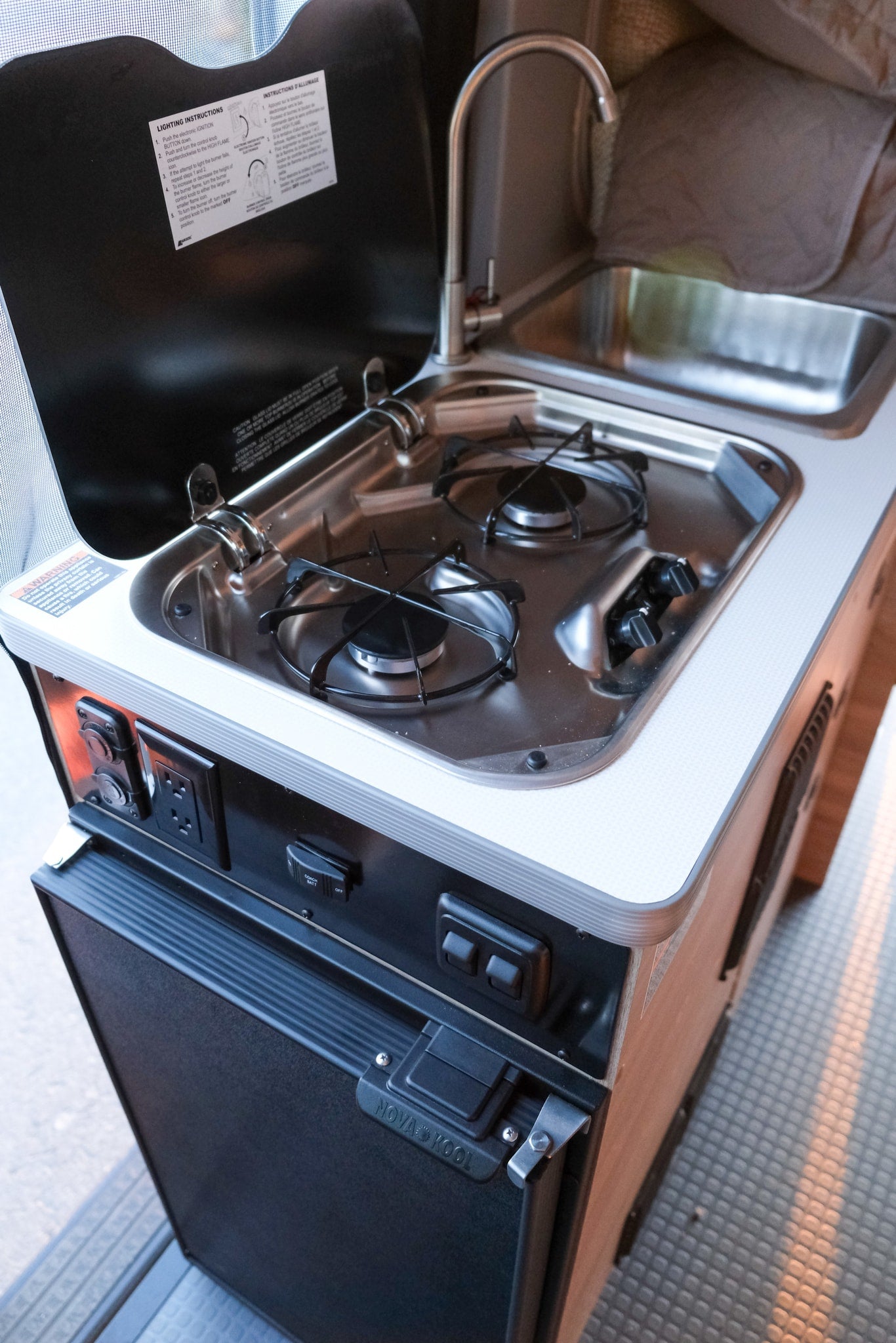 Compact RV rental kitchen: two-burner stove, sink, faucet, and Nova Kool fridge for convenient cooking on the go.