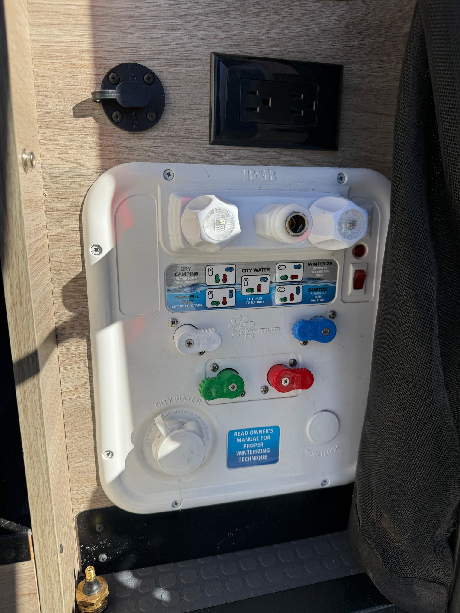 RV rental water control panel with settings for dry camping, city water, winterizing, and sanitizing modes. An electrical outlet is also present.