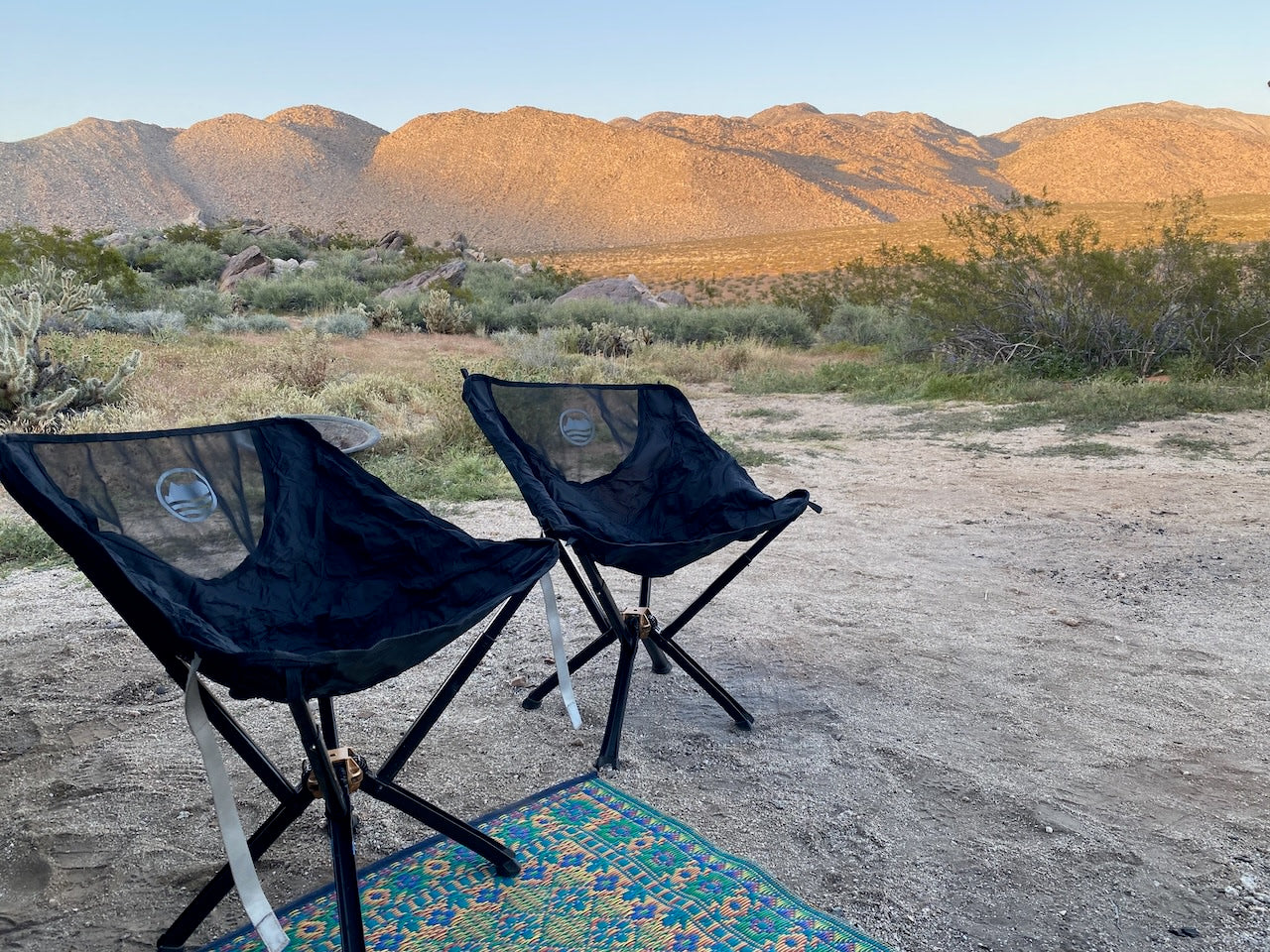 Relaxing at our RV rental desert campsite. Two chairs face golden mountains and open skies, perfect for outdoor travel.