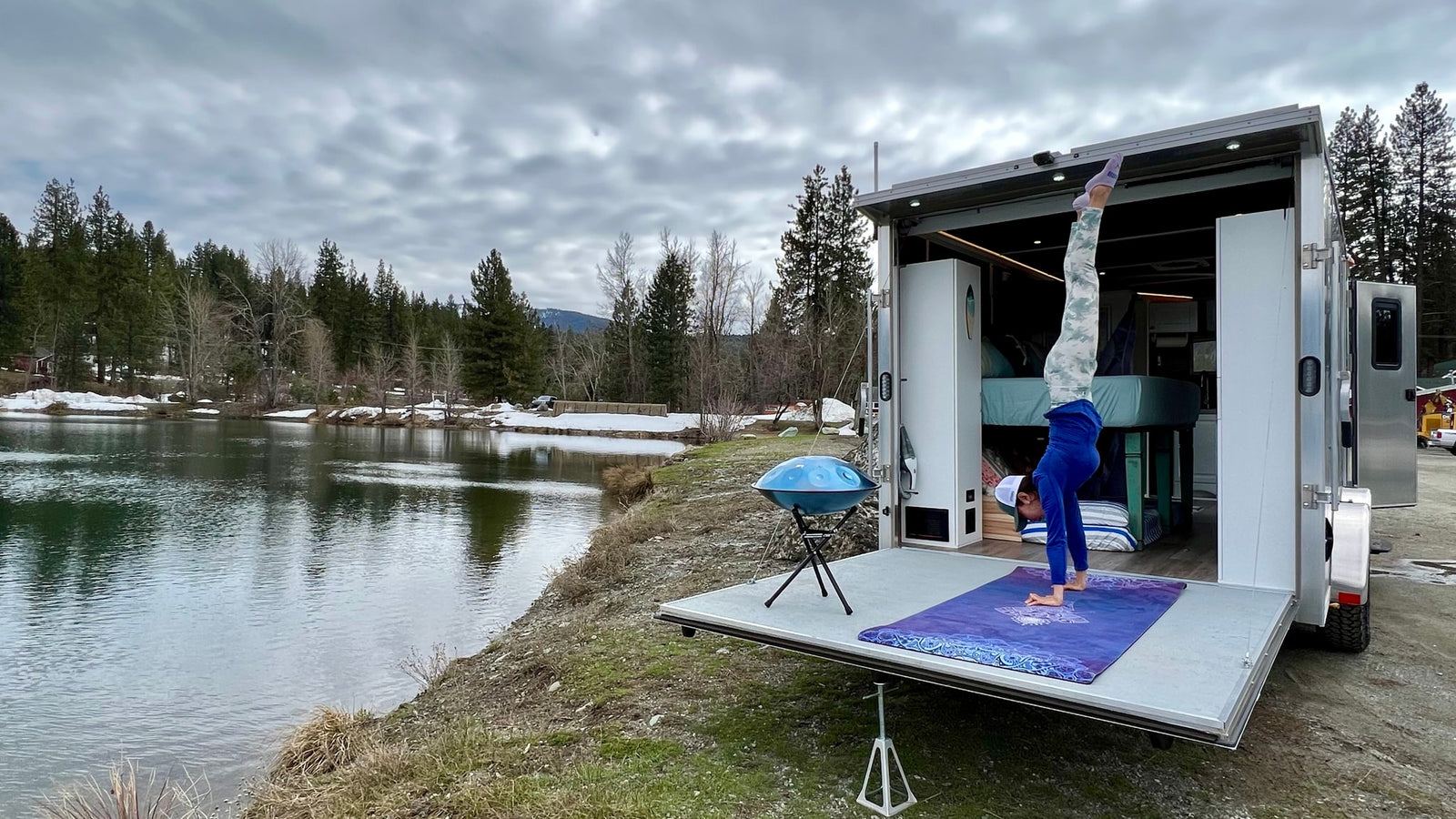 RV rental yoga: Person does handstand on camper ramp by a peaceful lake amidst trees. Great for nature lovers!