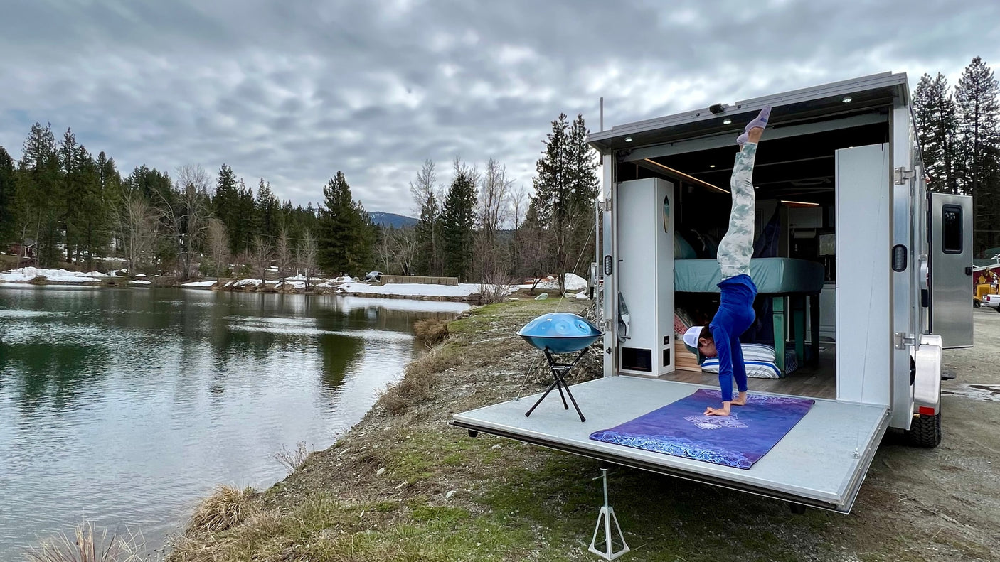 RV rental yoga: Person does handstand on camper ramp by a peaceful lake amidst trees. Great for nature lovers!