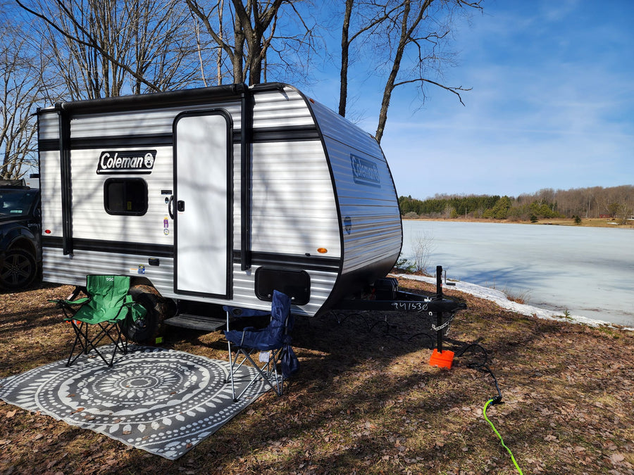 A Coleman travel trailer RV rental is set up for camping by a frozen lake