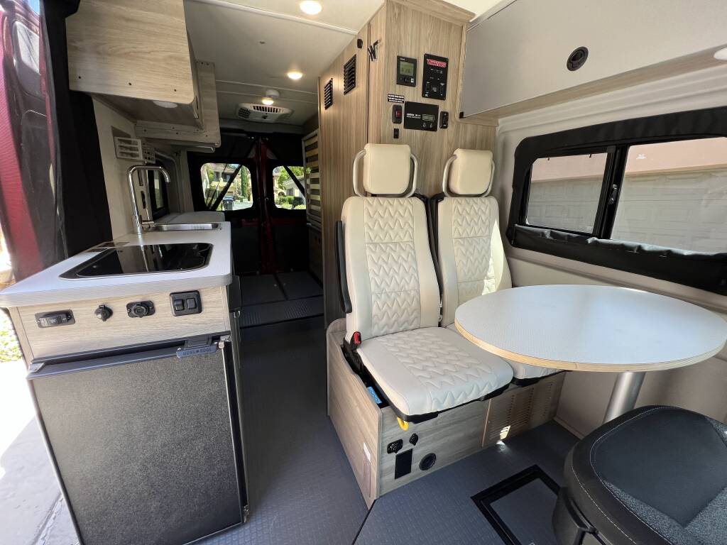 and table on a red rug at dusk.|This red camper van rv rental shows its open doors