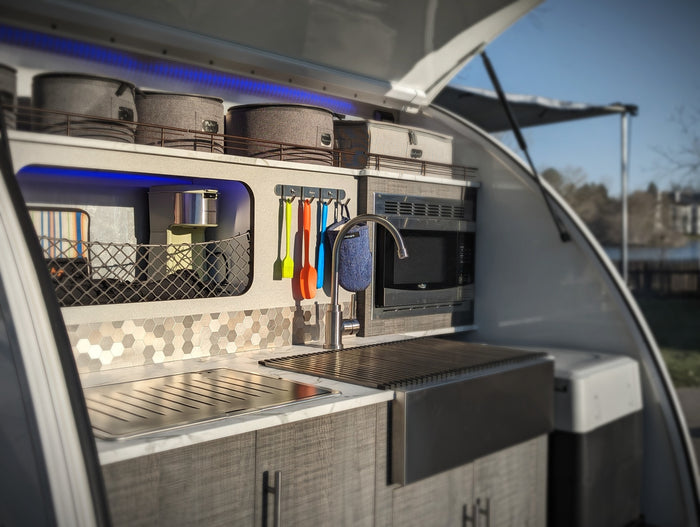 Sleek outdoor camper kitchen in an RV rental, showing a sink, microwave, and organized storage for camping trips.