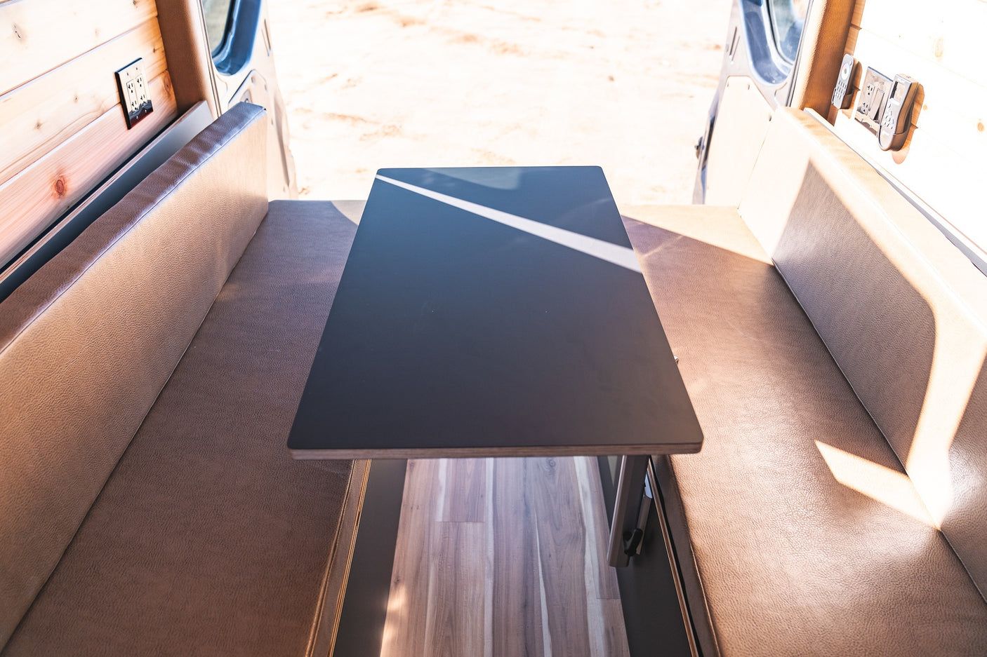 Modern RV rental interior: sleek table, comfy bench seating, wood paneling, and power for your next adventure.