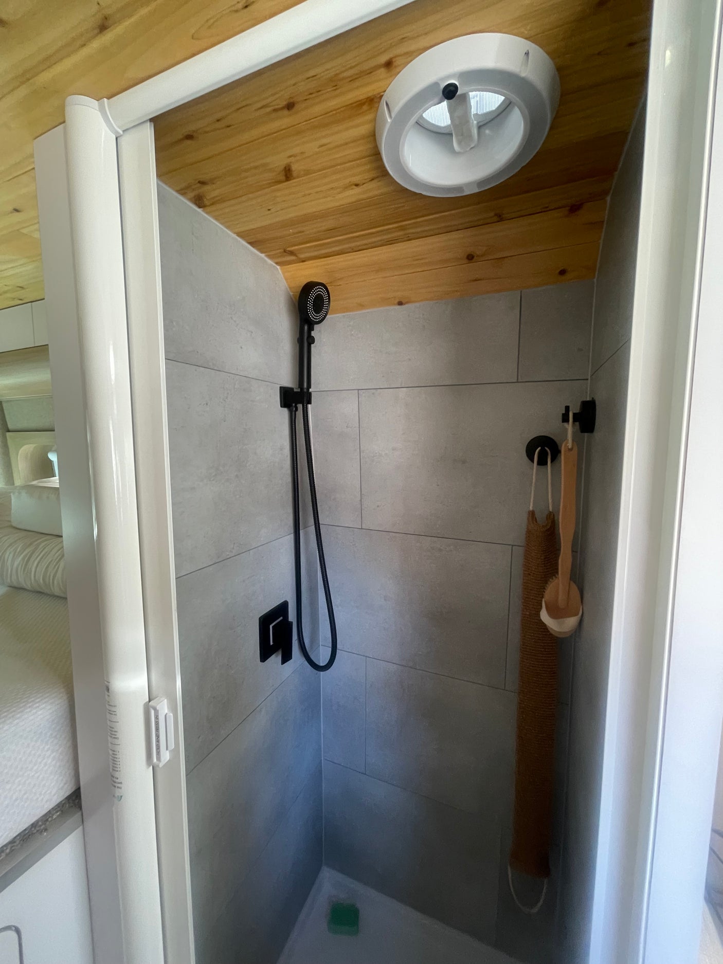 Modern tiled shower in a compact RV rental, featuring a black shower head, wood ceiling, and hanging bath accessories.
