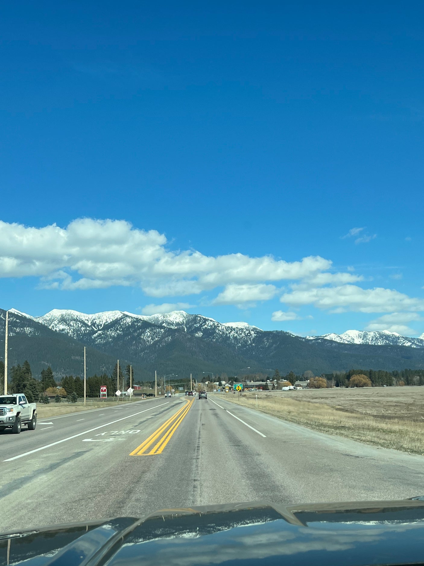 Road trip via RV rental: drive towards snow-capped mountains and a distant town under a clear blue sky.