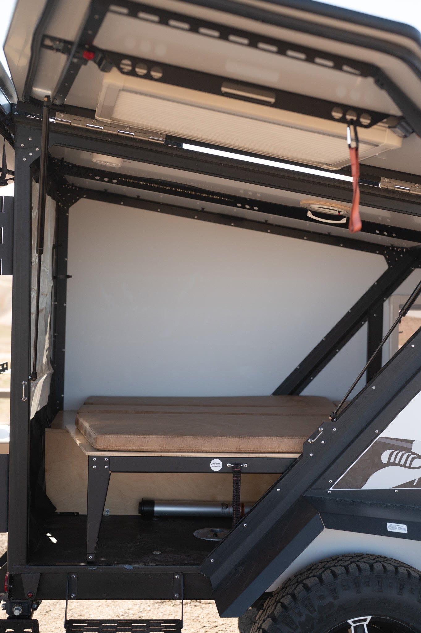 Inside a compact rv rental trailer: comfy bed cushions, light walls, and sturdy metal frame ready for adventure.