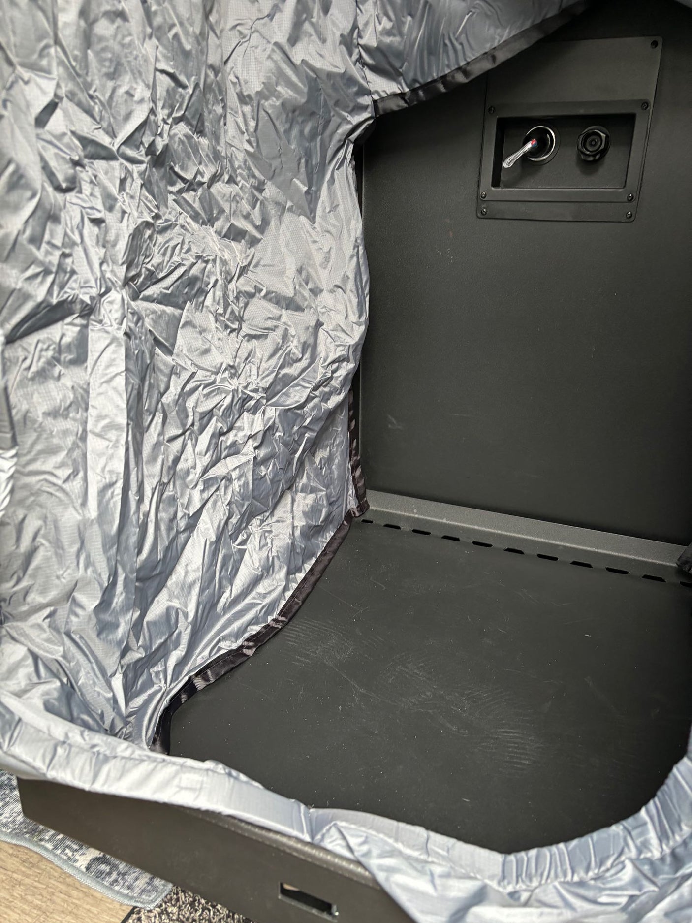 Inside a portable RV rental shelter: crinkled silver fabric, dark interior, and back panel controls for comfort.