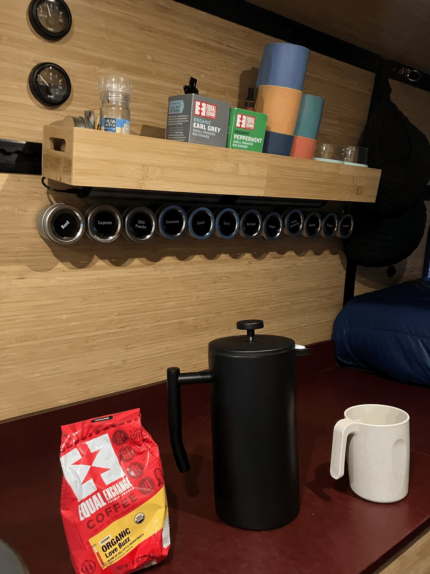 RV rental kitchenette with coffee, tea, and magnetic spices. Features a French press, colorful cups, and gauges, ideal for van life.