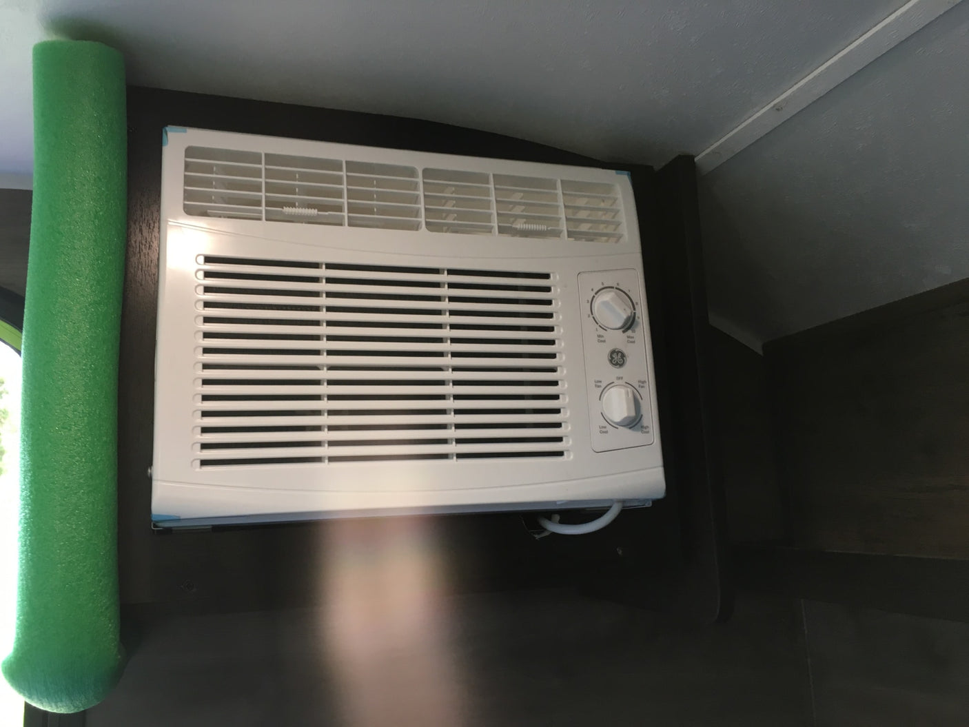 White GE air conditioner with control knobs and green foam insulation, seen inside an RV rental for cooling comfort.