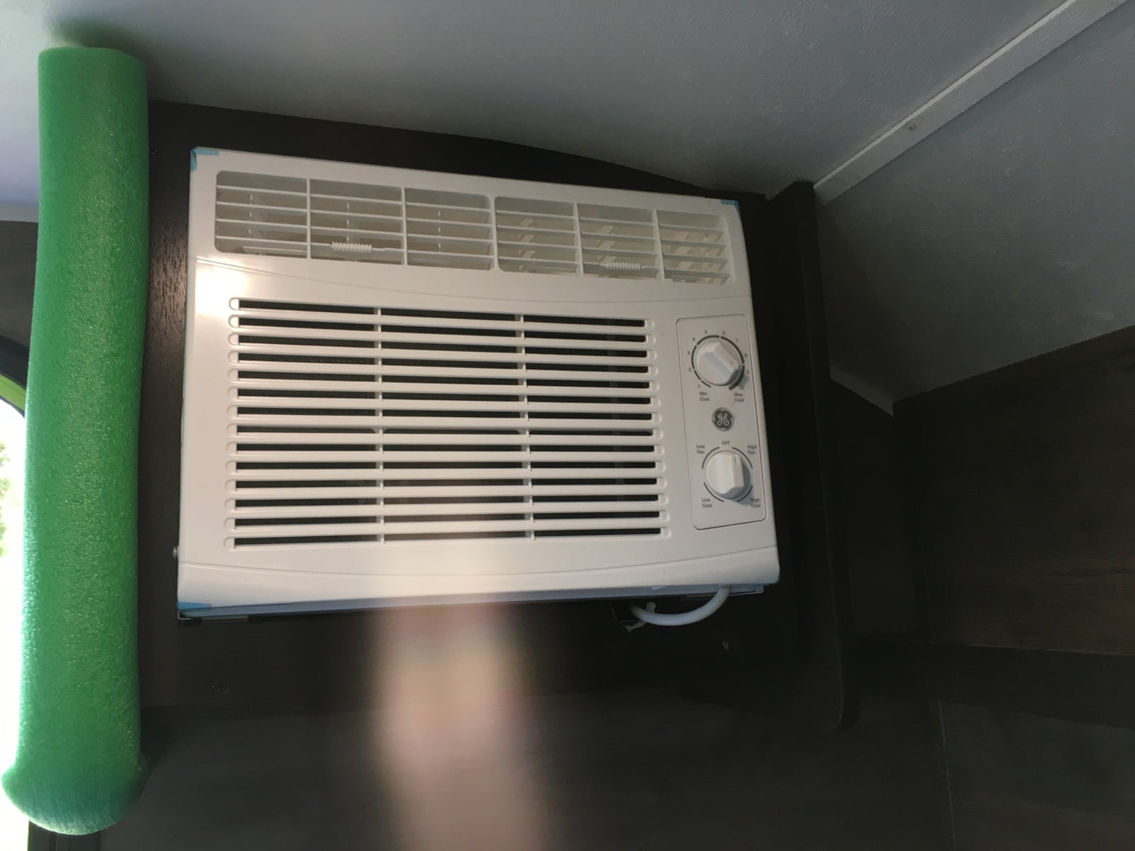 White GE air conditioner with control knobs and green foam insulation, seen inside an RV rental for cooling comfort.