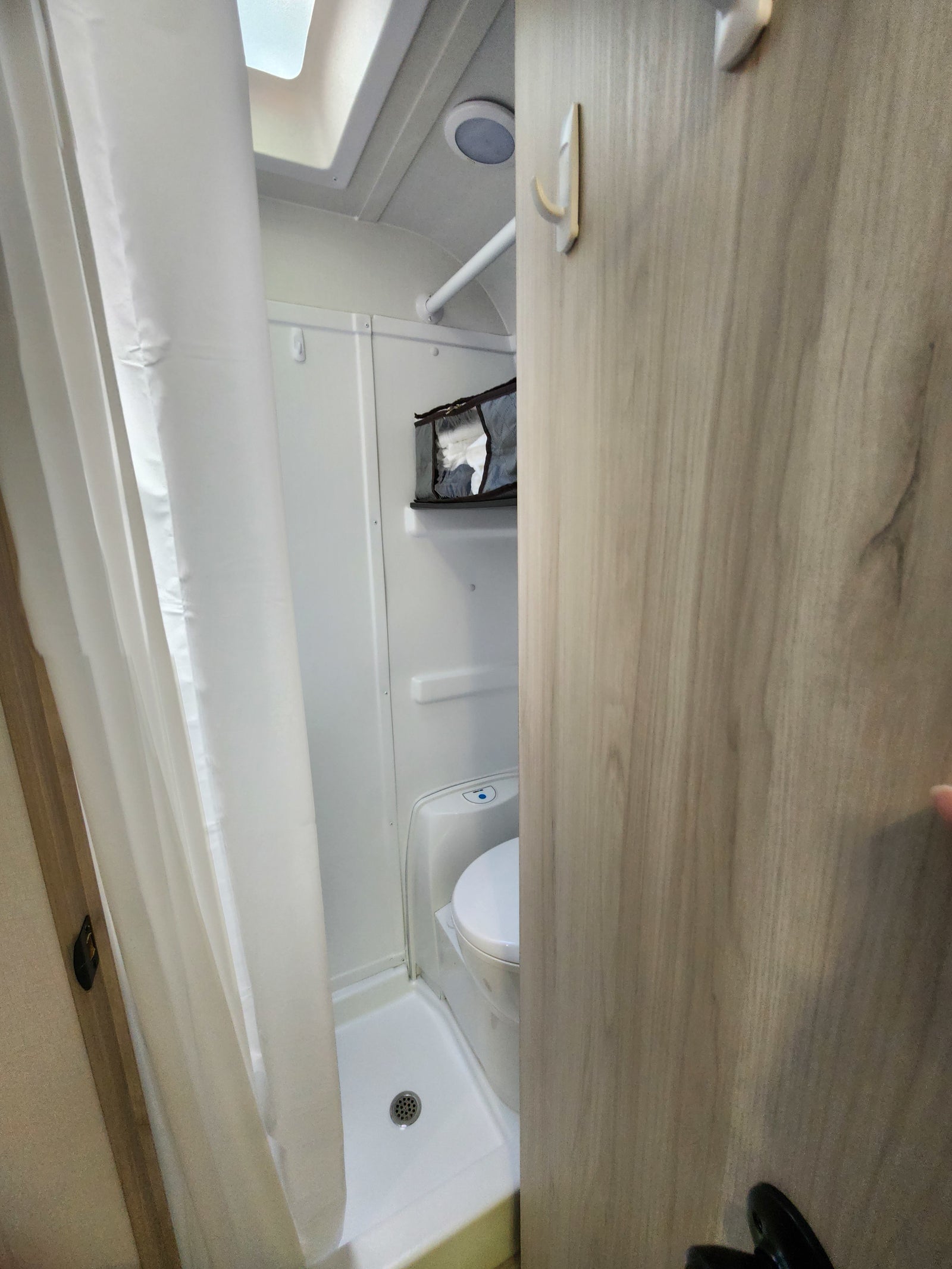 Compact RV rental wet bath, combining shower and toilet for efficient use of space, with hooks and storage.