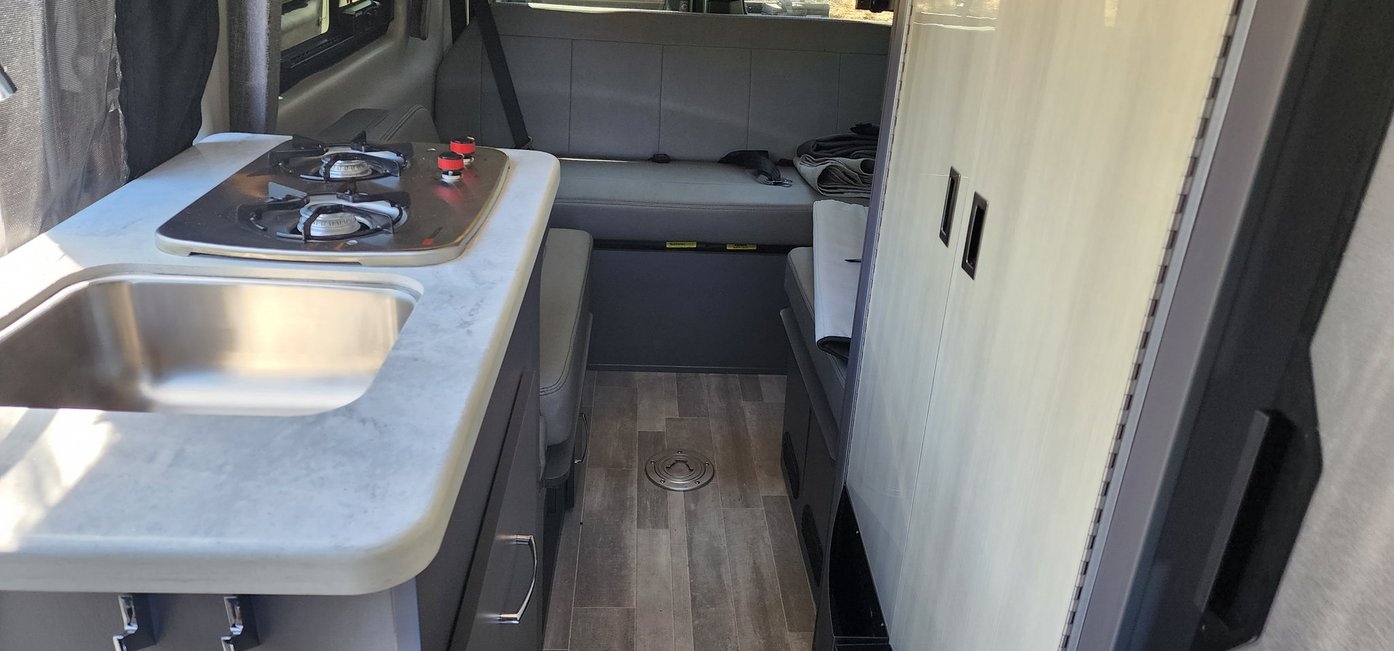 RV rental: Compact interior with kitchen (sink, 2-burner stove), flexible seating, and storage cabinetry for travel.
