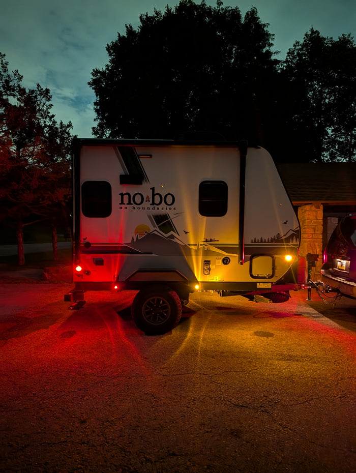 Illuminated RV rental at night, showcasing vibrant red and amber lights against a dark sky, perfect for camping.