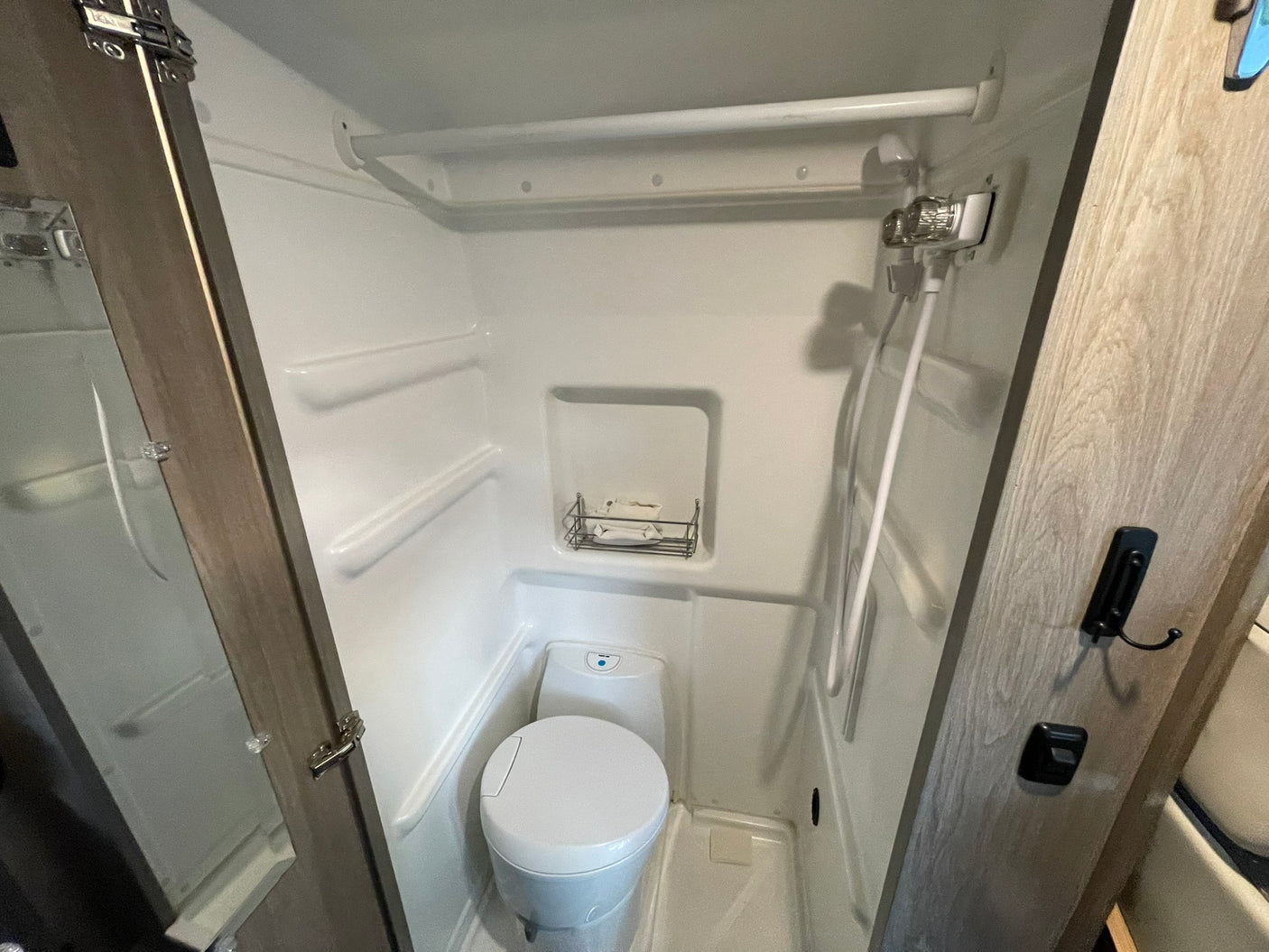 Compact rv rental bathroom: a white molded shower stall with a toilet, showerhead, and small wire shelf, designed for efficiency.