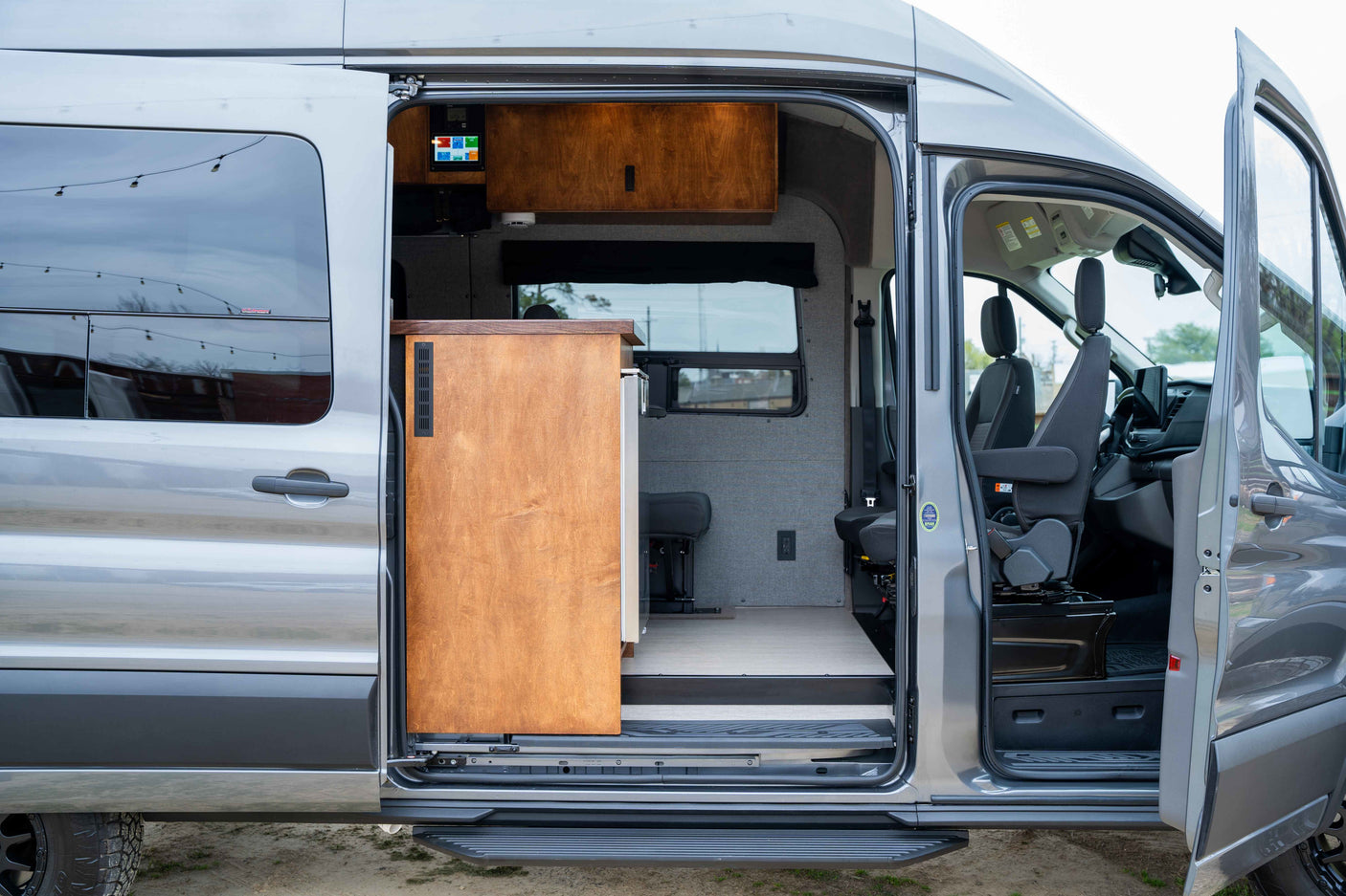 RV rental: See inside a modern camper van conversion with an open side door, showcasing its kitchen, control panel, & comfy seating.