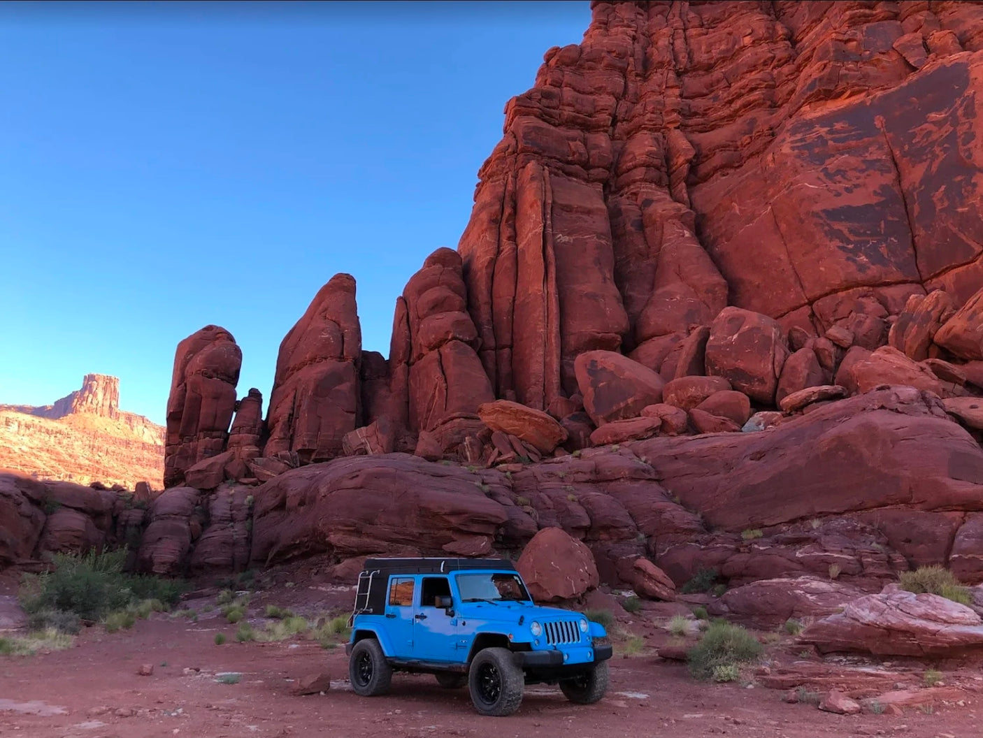 warms by a roaring campfire at dusk.|A blue Jeep