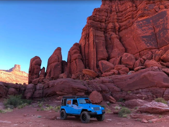 warms by a roaring campfire at dusk.|A blue Jeep