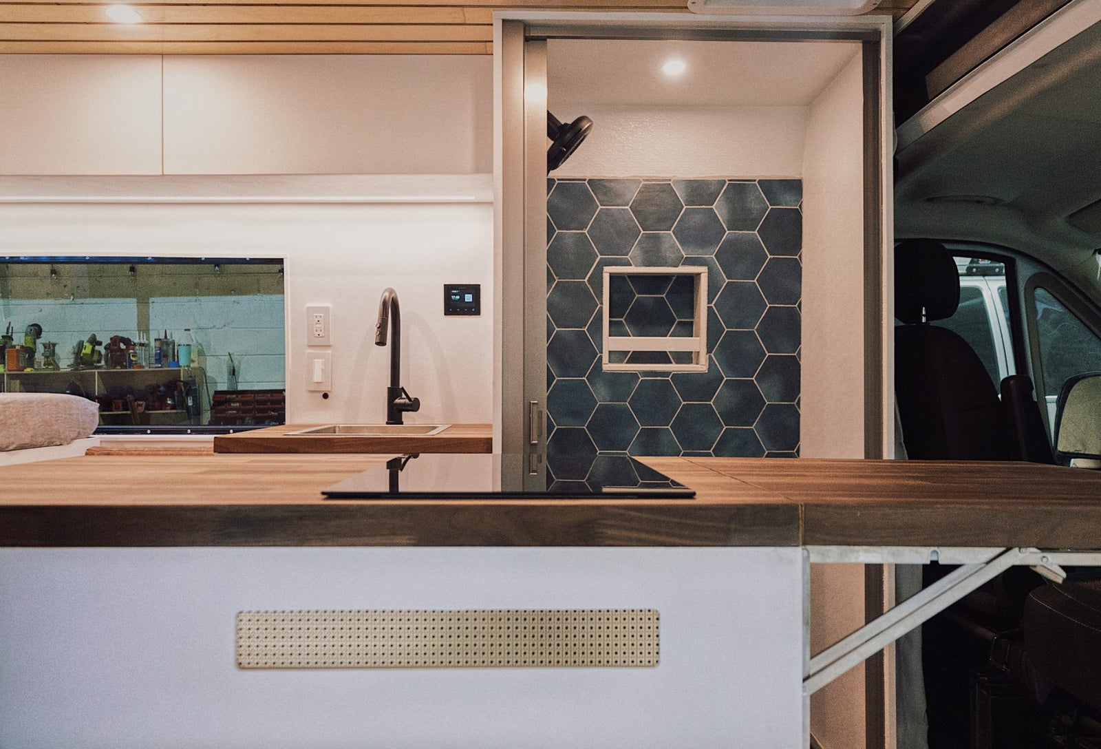 and a sleek black Nebia showerhead.|Interior view of an RV rental ceiling with a white fan/vent and light wood planks