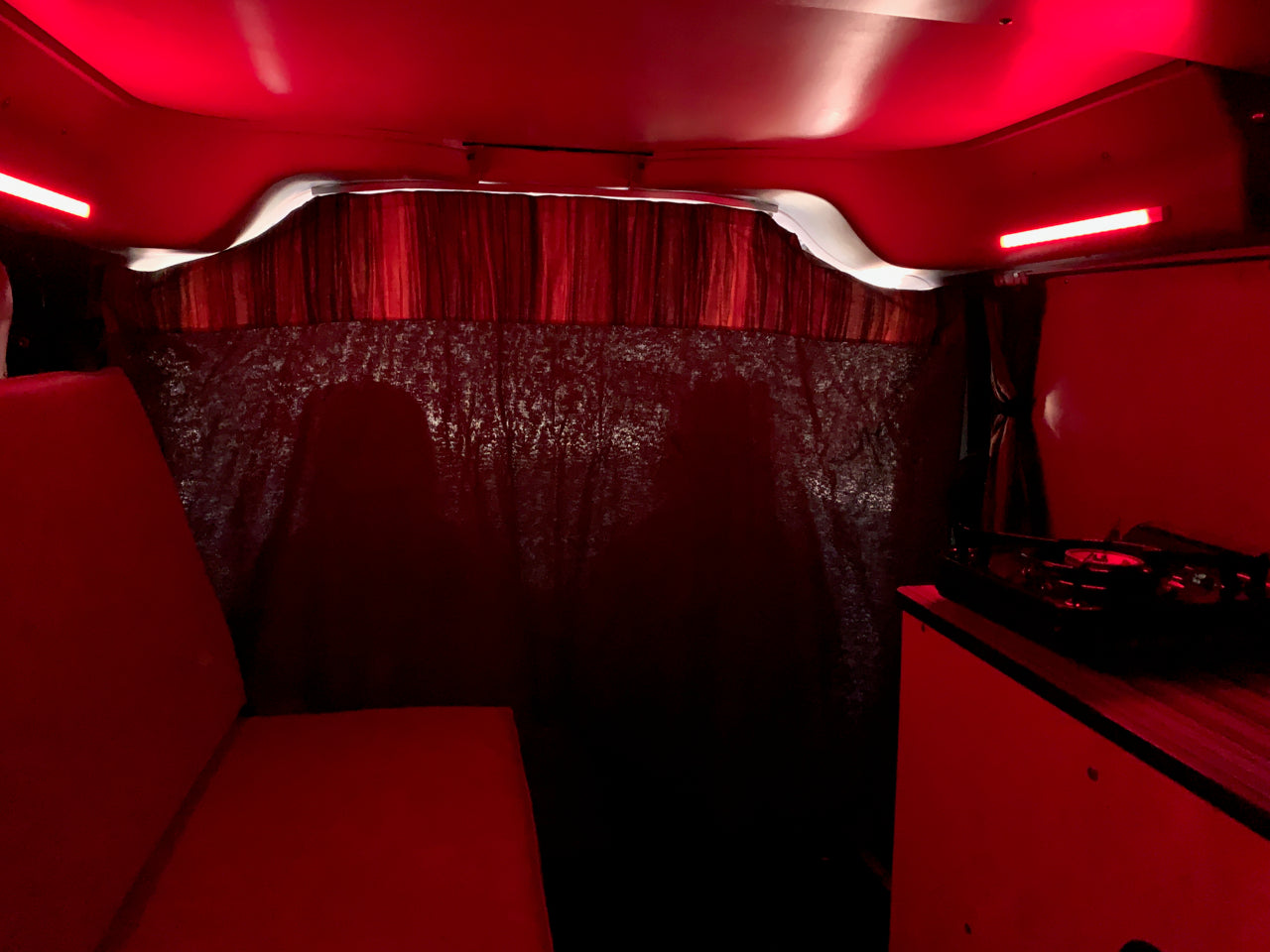 Inside a unique RV rental: red lights illuminate cozy seating, a DJ setup, and subtle shadows on patterned walls.