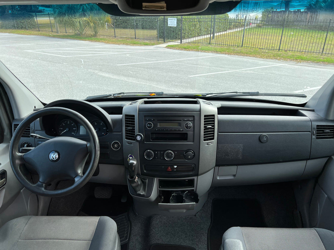 Inside an RV rental van: driver's perspective showing the dashboard, steering wheel, and view of a parking lot through the windshield.