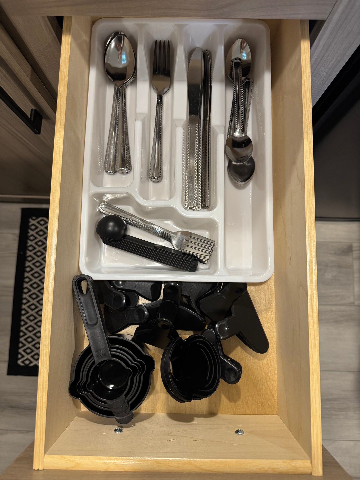 An RV rental kitchen drawer, neatly organized with silverware, measuring cups, and bag clips.