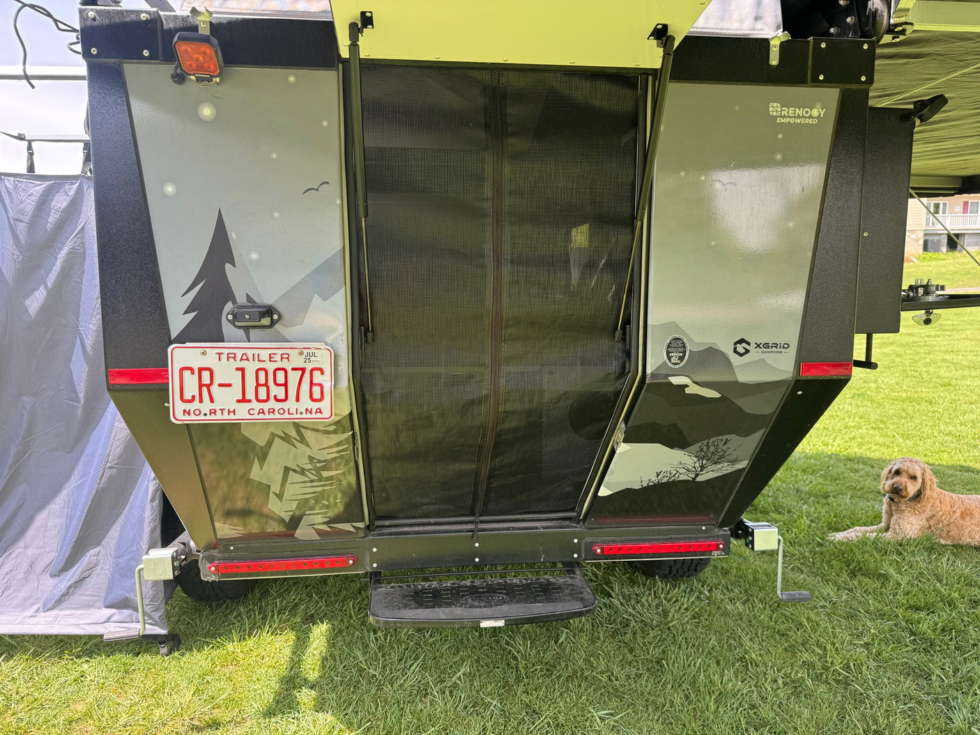 Rear view of an XGRID CAMPERS trailer, perfect for RV rental, with a North Carolina plate, nature graphics, and a dog resting.