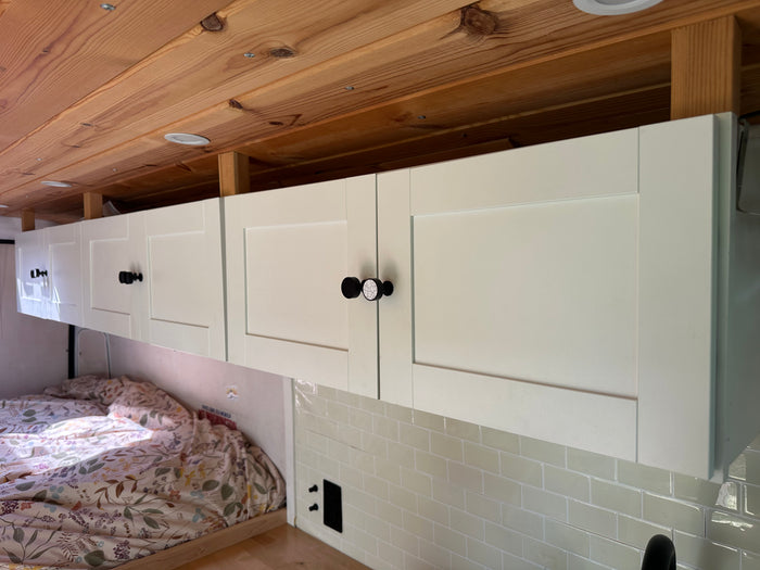 Cozy RV rental interior featuring light overhead cabinets, a warm wooden ceiling, and a comfortable bed area.