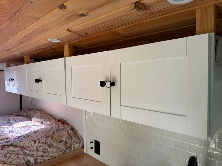 Cozy RV rental interior featuring light overhead cabinets, a warm wooden ceiling, and a comfortable bed area.