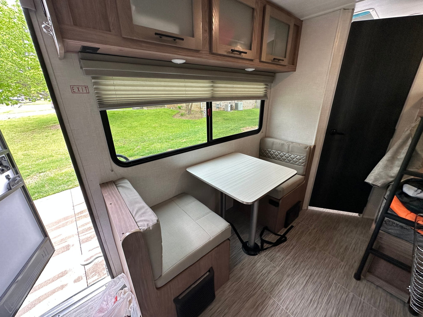 Interior of an RV rental: Dinette with table, padded benches, window view, and upper storage cabinets.