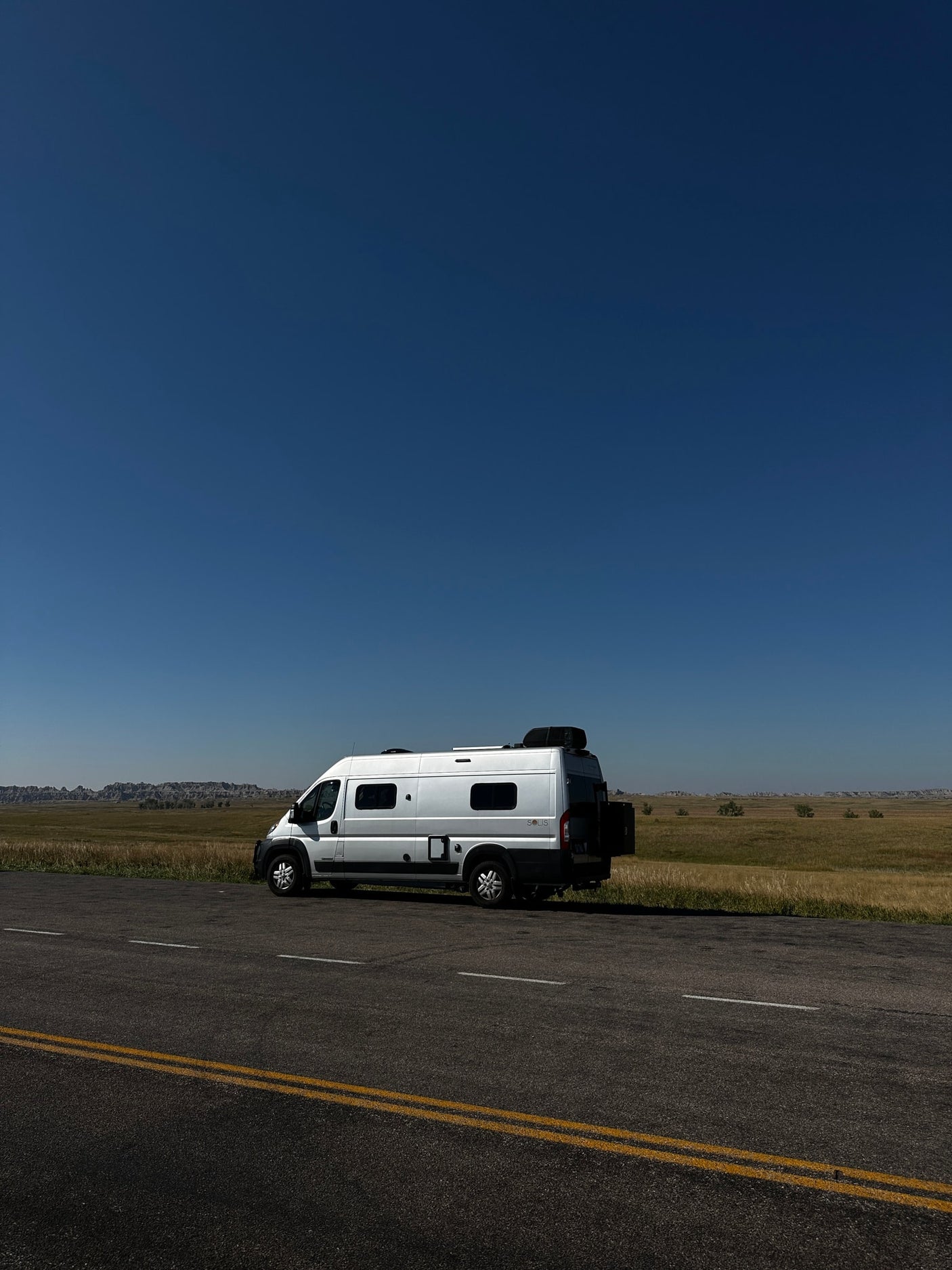 sunny landscape with hills. Perfect for your next adventure!|Cozy RV rental bed with open doors revealing epic badlands. Interior shows AC unit