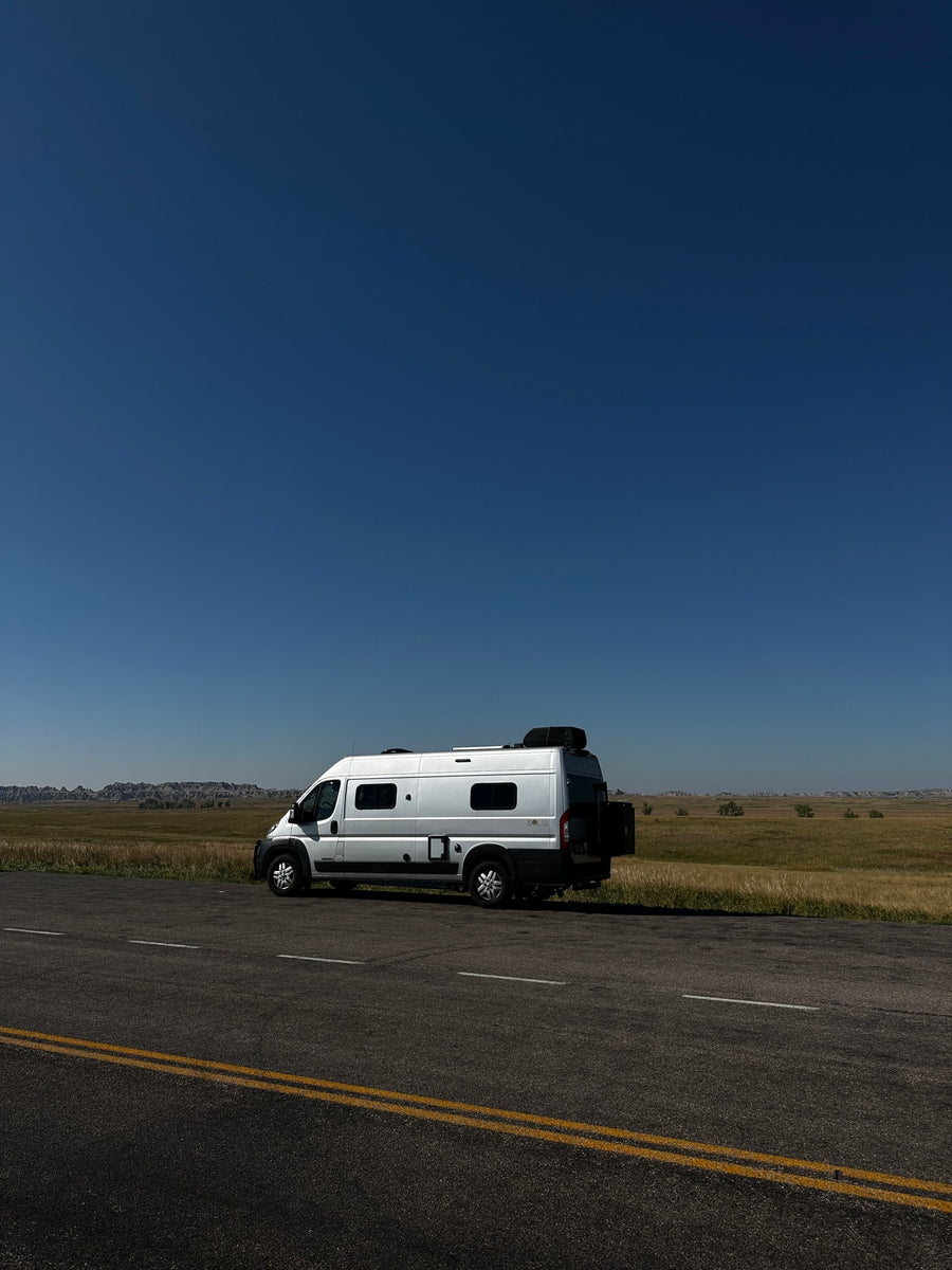 sunny landscape with hills. Perfect for your next adventure!|Cozy RV rental bed with open doors revealing epic badlands. Interior shows AC unit