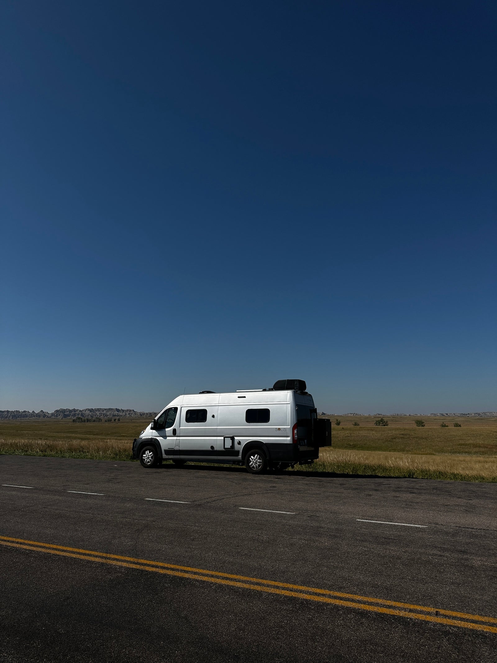 sunny landscape with hills. Perfect for your next adventure!|Cozy RV rental bed with open doors revealing epic badlands. Interior shows AC unit