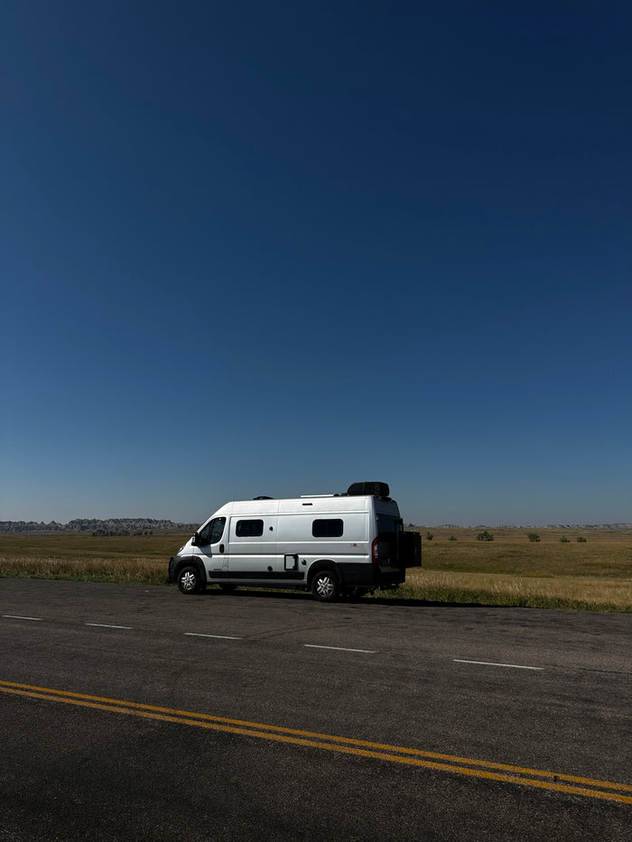 sunny landscape with hills. Perfect for your next adventure!|Cozy RV rental bed with open doors revealing epic badlands. Interior shows AC unit
